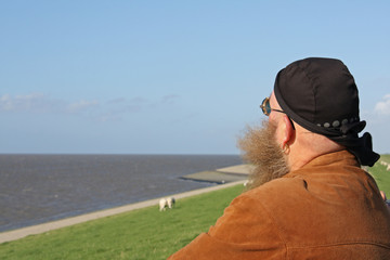  Mann mit langem Bart, der vom Wind verwirbelt wurde, steht am Ufer des Meeres