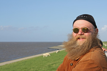  Mann mit langem Bart, der vom Wind verwirbelt wurde, steht am Ufer des Meeres