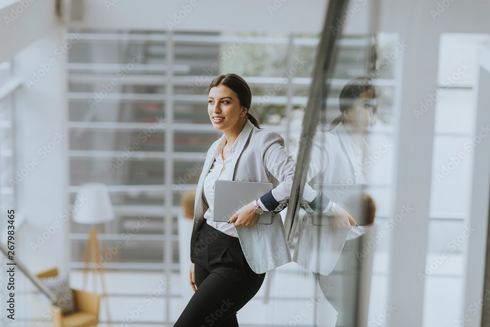 Wall mural young business woman stands on the stairs at the office and use mobile phone