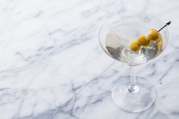 Martini cocktail with green olives on marble table background. Copy space.