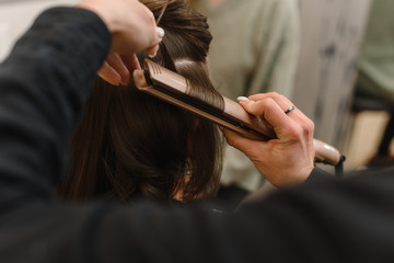 Hairdresser curls hair with a hair straightener. Master creates a hairstyle girl.