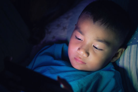 Asian Child Using Smartphone At Night On The Bed In Dark Room, Using Smartphone In Dark May Be Causes Of Eye Pain Symptom,Health Concept