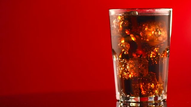 Coke with ice cubes closeup. Glass of fizzy cola rotated over red background. 4K UHD video footage. 3840X2160