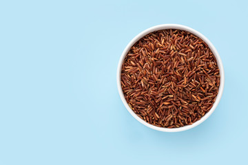 Raw red rice in a white bowl on a blue background. Top view, copy space, minimalistic.