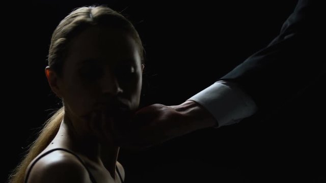 Cruel man looking at beautiful face of young woman on black background, trade