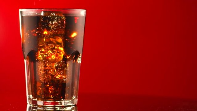Coke with ice cubes closeup. Glass of fizzy cola rotated over red background. 4K UHD video footage. 3840X2160