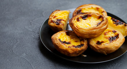 Egg tart, traditional Portuguese dessert, pastel de nata, pasteis on a plate. Grey stone background. Copy space.