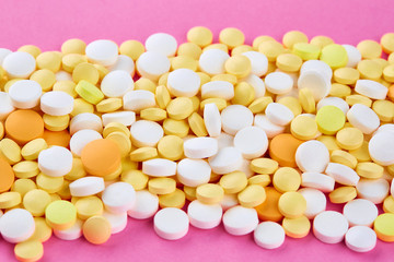 Fototapeta na wymiar Heap of white yellow and orange pills on pink background
