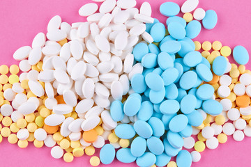Heap of white yellow blue and orange pills on pink background