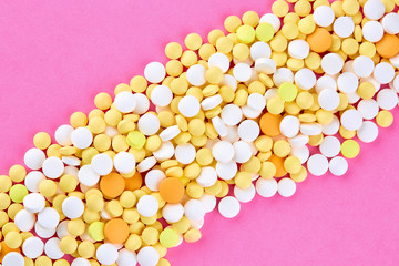 Heap of white yellow and orange pills on pink background