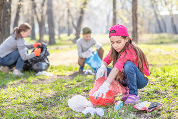 Young girl picking up trash in the park. Volunteer concept