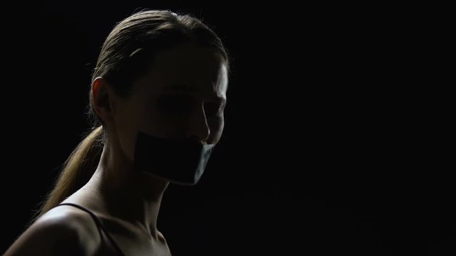 Male hands taping mouth of young woman, slavery, humiliation of female rights