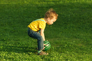 Cute positive kid, playing happily with ball on green meadow