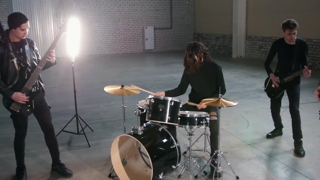 A rock group having a repetition. A man with cool long hair playing drums
