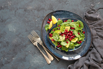 Healthy vegetarian avocado salad with spinach, pomegranate and sesame in a plate on dark background. Top view with copy space.