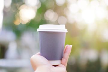Coffee in a gray  paper cup on male hand holding. Beautiful Natural park green blur and bokeh background. Sunlight and flare  concept.
