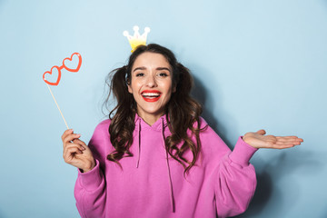 Portrait of joyful princess girl wearing paper crown laughing and holding funny sunglasses on stick