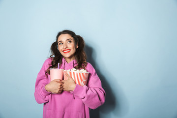 Portrait of happy young woman with two ponytails holding soda beverage in plastic cup and popcorn bucket