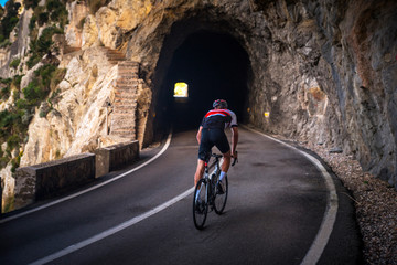 Man on road bicycle ride on the road in mountains. Dark rocky tunnel on the Road. Sa Calobra, Majorca, Spain