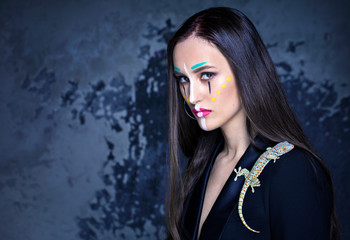 model in a bright make-up with a lizard on a jacket and on a dark blue background of Studio