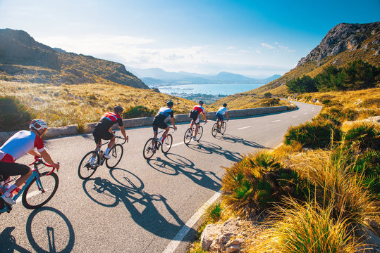 Group of cyclist ride together on road bicycles in beautiful nature. Sunset light, sea in background.
