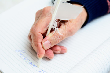 In the hand of an elderly woman's quill pen, with which she writes in a notebook