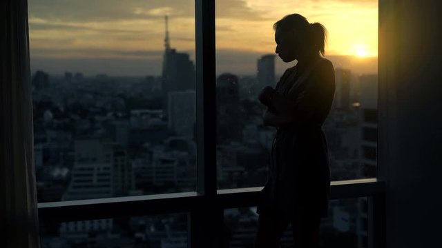 Sad, desperate woman by window at home during sunset