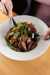 Restaurant salad on a white plate with female hands