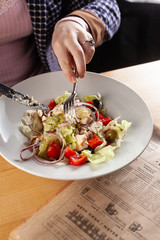 Summer salad on a white plate with female hands holding flatware