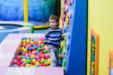 Fototapeta na wymiar Happy boy having fun in ball pit in kids amusement park and indoor play center. Child playing with colorful balls in playground