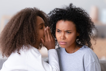 African American teen daughter whispering in unhappy mother ear