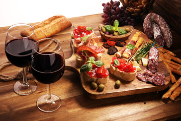 Fototapeta na wymiar Traditional italian antipasto bruschetta appetizer with cherry tomatoes, cream cheese, basil leaves and balsamic vinegar on cutting board with prosciutto, salami, cheese