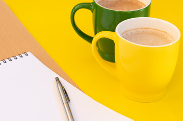 Paper notepad and two cups cappuccino on the yellow background.