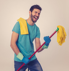 Young attractive proud man holding mop as microphone having fun while cleaning