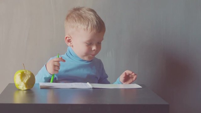 two year old boy is drawing with marker at album and eating apples