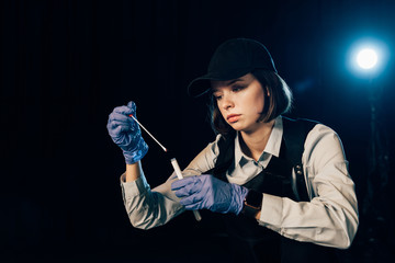investigator in rubber gloves holding swab and test tube at crime scene