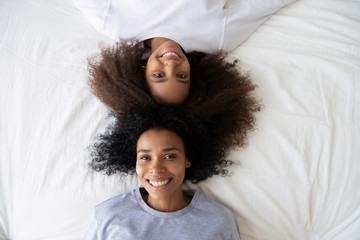 Top view African American teen daughter lying on bed with mother