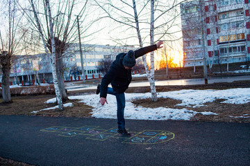 A young man playing hopscotch on asphalt. Good mood and spring in Russia. A bearded man recalls his childhood.