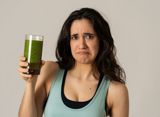 Beautiful young sports latin woman boring of diet holding green smoothie in dislike