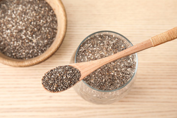 Glass of water with chia seeds and spoon on wooden background, top view