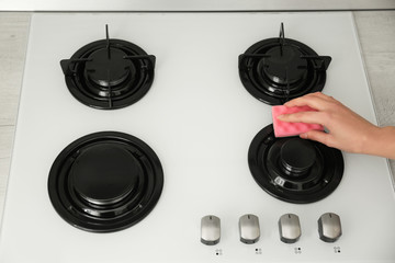 Woman cleaning gas stove with sponge, closeup