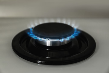 Gas burner with blue flame on modern stove, closeup