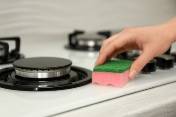 Woman cleaning gas stove with sponge, closeup