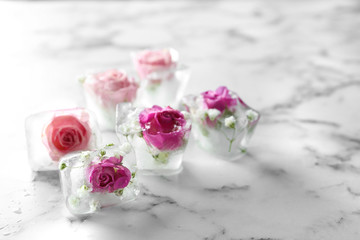 Ice cubes with roses on marble background, space for text