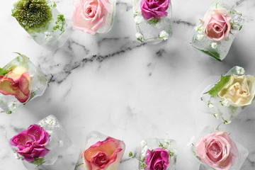 Frame made of ice cubes with flowers on marble background, flat lay. Space for text