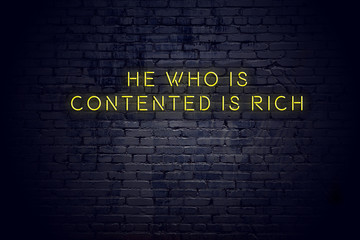 Neon sign with positive wise motivational quote against brick wall 