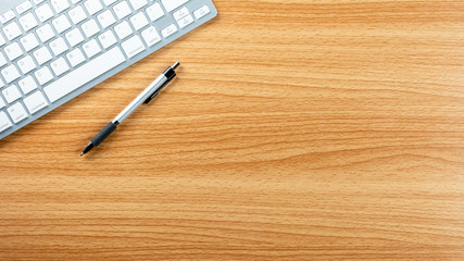 pen and computer keyboard on wooden desk background.
