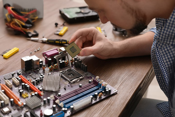 Fototapeta na wymiar Male technician repairing motherboard at table, closeup
