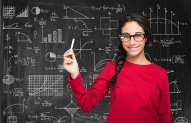 Young teenager holding a chalk and resolving complex formulas on a blackboard