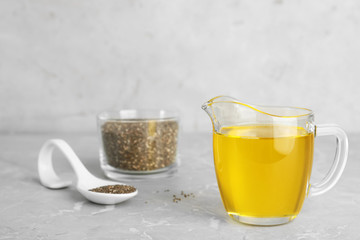 Composition with jug of chia seeds oil and grains on grey table. Space for text